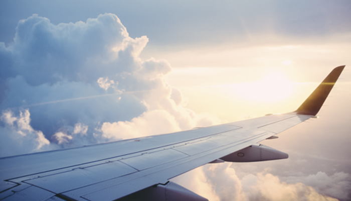 Flügel eines Flugzeuges in der Luft mit Wolkenhimmel und Sonne